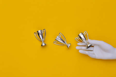 White mannequin hand holding championship cups on yellow background. top viewの写真素材