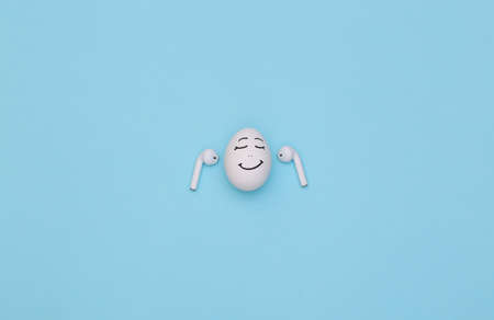 Chicken egg happy face listen music with wireless headphones on a blue background.