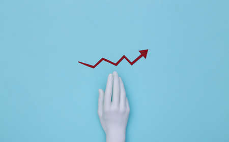Mannequin's hand and red growth arrow tending upward on a blue background.の写真素材
