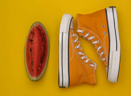 Slice of ripe watermelon and sneakers on yellow background. top view. flat layの写真素材