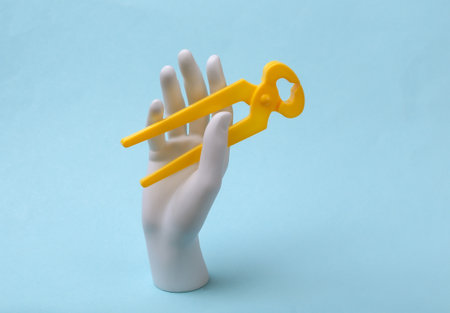 White mannequin hand holds forceps on blue background. Renovation concept, industry. minimalismの写真素材