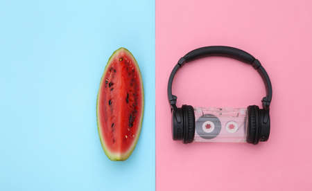 Slice of ripe watermelon and stereo headphones with retro audio cassette on pink blue background. summer fun. top view. flat layの写真素材