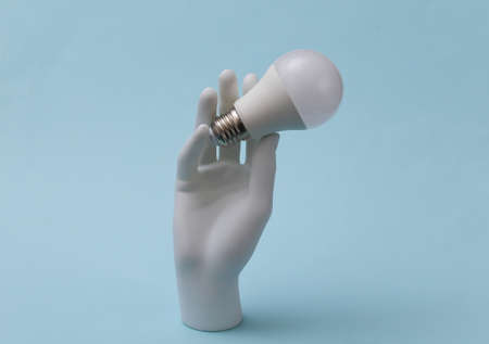 A white mannequin hand holds a led light bulb on a blue background. I have an idea! Eco conceptの写真素材