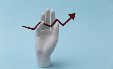 A white mannequin hand holds a growth arrow pointing upwards on a blue background. business, economy conceptの写真素材