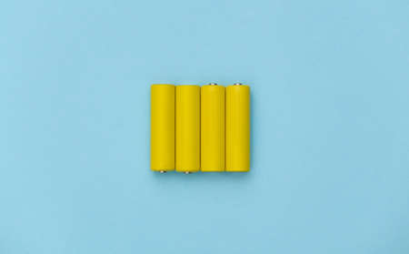 Four yellow AA batteries on blue pastel background. top view