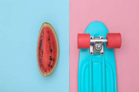 Slice of ripe watermelon and cruiser board on pink blue background. summer fun. top viewの写真素材