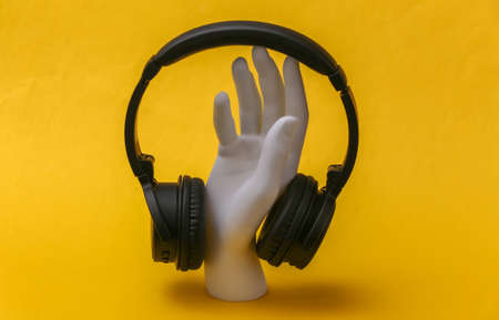 White mannequin hand with headphones stands on yellow background.の写真素材