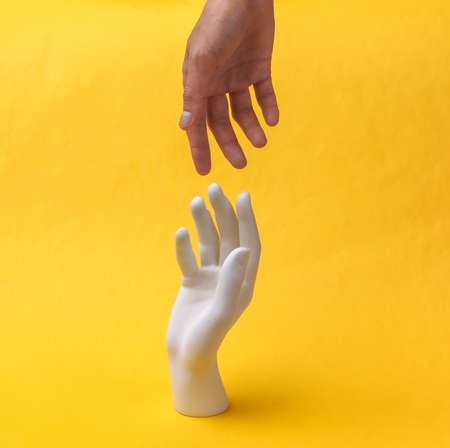 Human Hand reaching for the mannequin hand on a yellow background. minimalismの写真素材