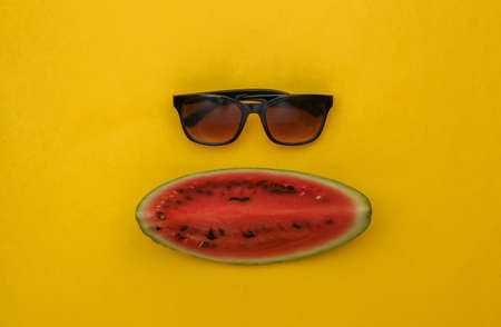 Slice of ripe watermelon and sunglasses on yellow background. summer fun. top view. flat layの写真素材
