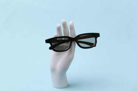 White mannequin hand holds 3d glasses on blue backgroundの写真素材
