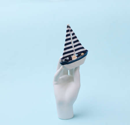 White mannequin hand holds boat on blue background. travel conceptの写真素材