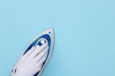 White mannequin hand holds iron on blue background. top viewの写真素材