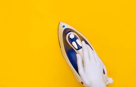 White mannequin hand holds iron on yellow background. top viewの写真素材