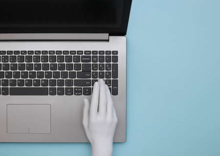 Mannequin hand typing on laptop keyboard. blue background. Top view, minimalism