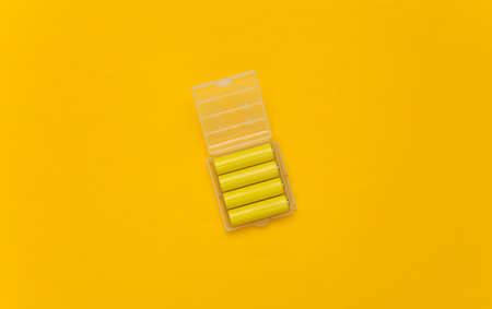 Four yellow AA batteries in plastic box on yellow background. top viewの写真素材