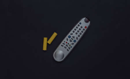 Tv remote and two batteries on black background. top view