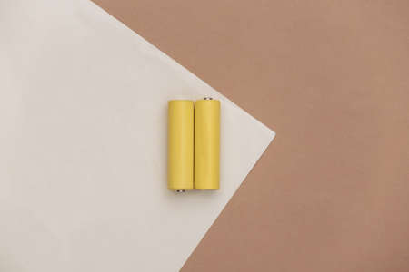 Two yellow AA batteries on brown beige background. top view