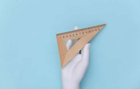 White mannequin hand holding wooden school triangle ruler on blue pastel background.の写真素材