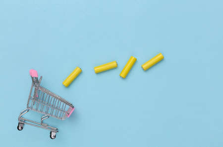 Shopping trolley with Four yellow AA batteries on blue background. top viewの写真素材