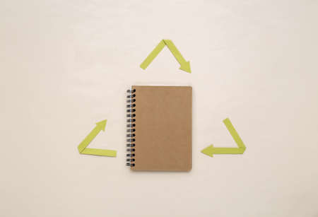 Recycled arrows sign and notebook on beige background. Eco concept. top viewの写真素材