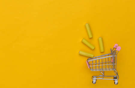 Shopping trolley with Four yellow AA batteries on yellow background. top view