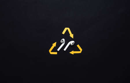 Recycled arrows sign and wireless headphones on black background. top view