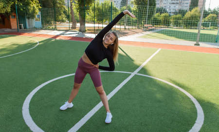Fit woman in sportswear doing pre-training warm-up, hand stretching at the stadium. Healthy...