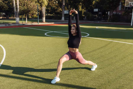 Fit woman in sportswear doing pre-training warm-up, body stretching at the stadium. Healthy...