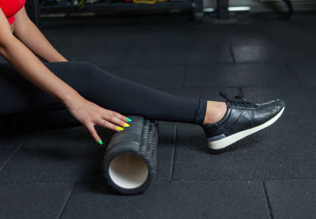 Fit woman using a foam roller to relieve sore muscles after a workout in modern gymの写真素材