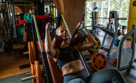 Young attractive woman practicing squats in exercise machine at gym