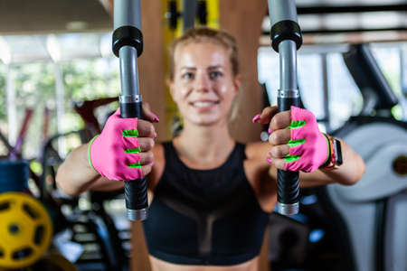 Young blond woman training upper body using fly machine in gym. Focus on hand