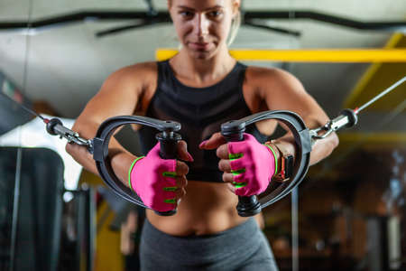 Young blond fit woman execute exercise with exercise machine Cable Crossover in gym. Focus on handsの写真素材