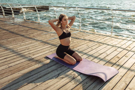 Fitness sport woman relaxing on the beach, listening music in headphone at sunrise