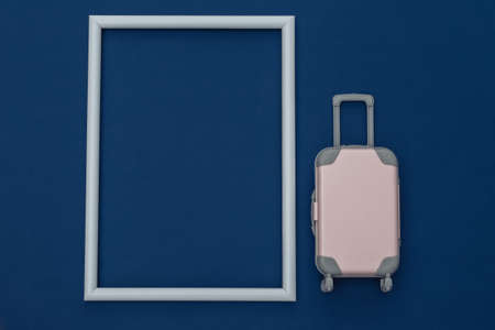 travel concept. Mini plastic travel suitcase on classic blue background with white frame for your text. minimal style. copyspace. top view, flat layの写真素材