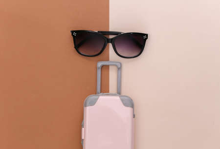 Travel or trip concept. Pink plastic travel suitcase toy and sunglasses on a beige brown background. minimal style. top view. flat layの写真素材