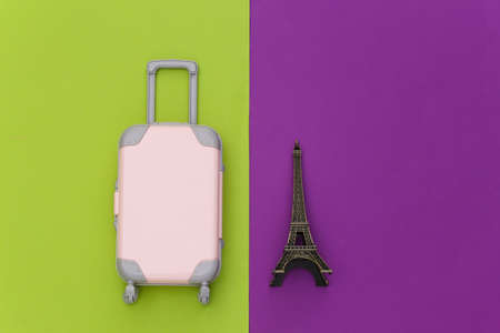 Traveled to Paris. Mini plastic travel suitcase and statuette of the Eiffel Tower on green purple background. top view. flat layの写真素材