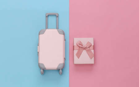 travel concept. Mini plastic travel suitcase and gift boxes on pink blue pastel background. minimal...