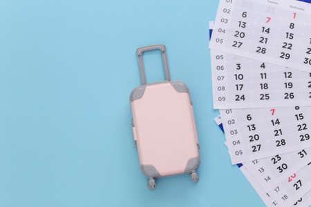 Time to travel. Mini plastic travel suitcase and monthly calendar on blue background. minimal style. top view. flat layの写真素材