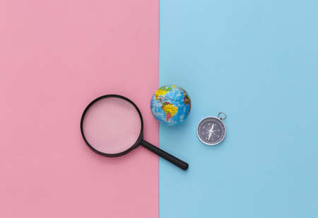 Minimalism travel, adventure flat lay. Compass and magnifier, globe on a blue-pink pastel background. top view.の写真素材