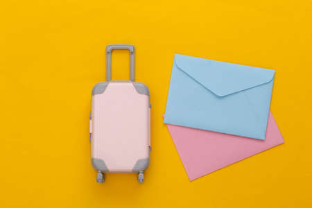 travel concept. Mini plastic travel suitcase and envelopes on yellow background. minimal style. top...