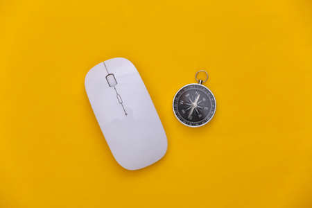 Compass and pc mouse on yellow background. Online business or travel. top view