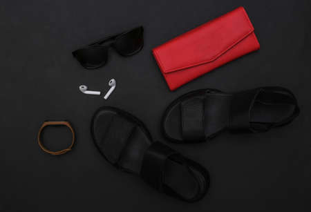 Gadgets and women's accessories on a black background. Sandals, smartphone, headphones, sunglasses, smart bracelet and wallet. top view. flat layの写真素材