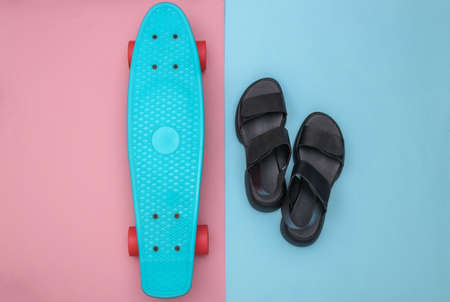 Flat lay composition of mini cruiser board and sandals on pink blue background. top view