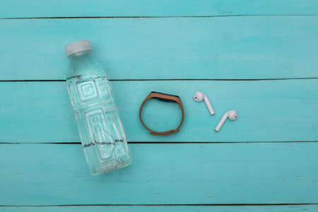 Fitness, sports minimalistic flat lay. Water bottle, wireless headphones and smart bracelet on blue...