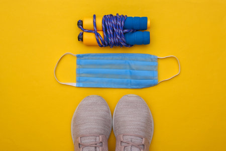 Fitness training during the covid-19 period. Flat lay composition of sneakers, skipping rope, medical mask on yellow background. Healthy lifestyle concept. top viewの写真素材