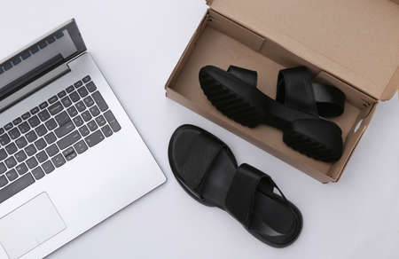 New sandals in a box and a laptop on a white background. top view
