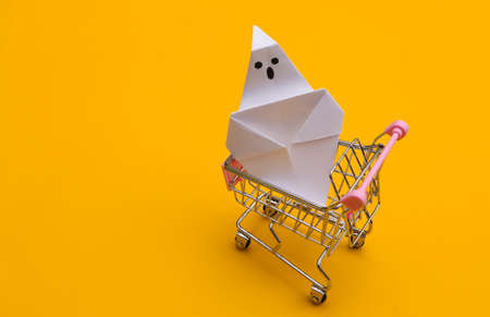Mini shopping cart with origami ghost on a yellow background. Halloween themeの写真素材