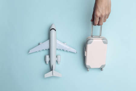 Hand holds mini puppet travel luggage and air plane on blue background. Travel time. top viewの写真素材