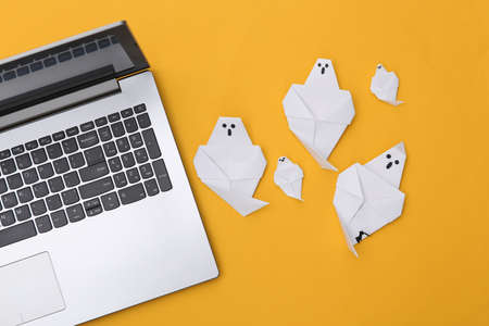Laptop and origami ghosts on yellow background. Halloween theme. top view