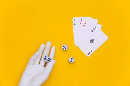 Dice in a white mannequin hand and four aces on a yellow background. top view